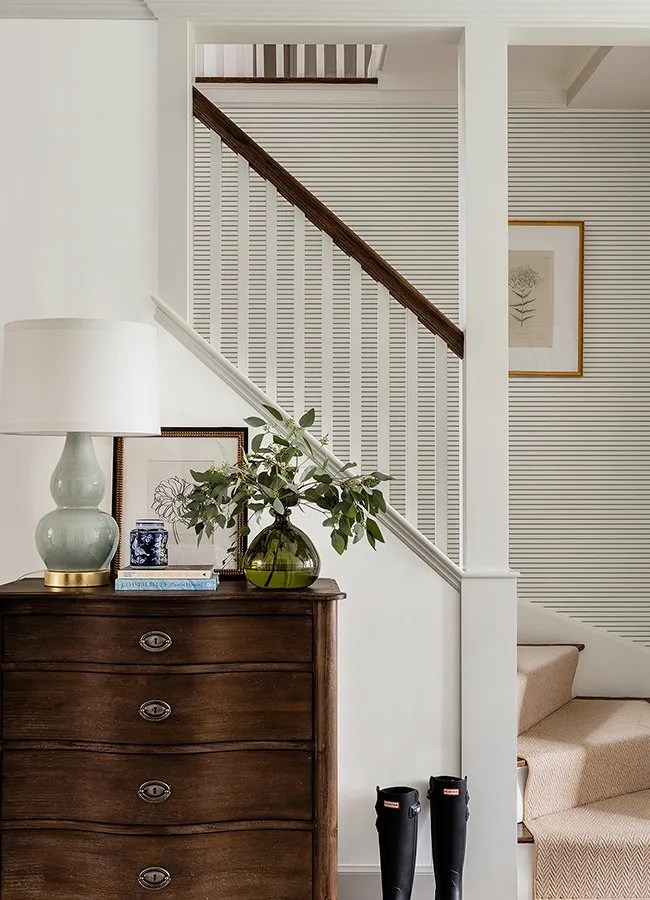 Plain green, grey and black horizontal striped wallpaper in the hallway and staircase with vintage chest of drawers. 