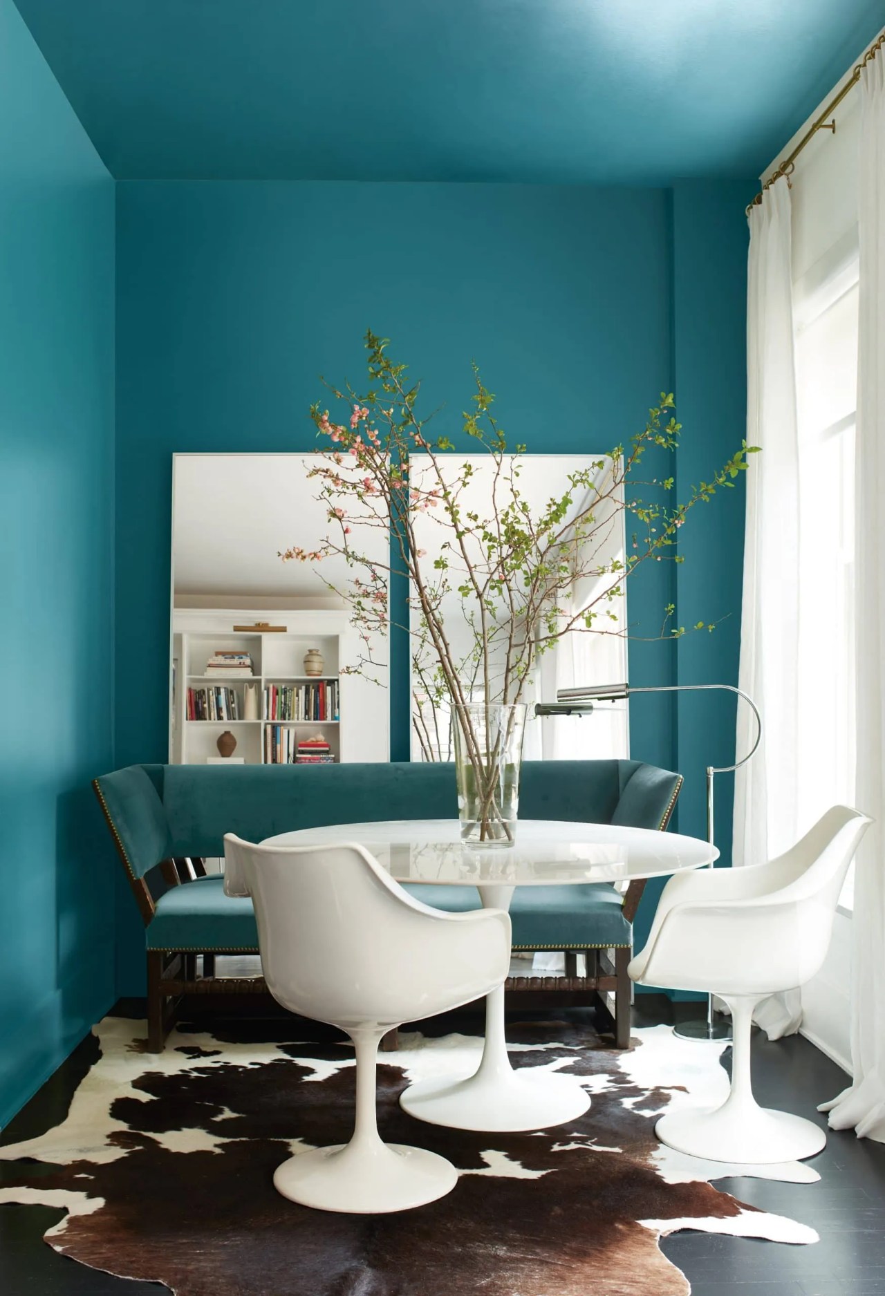 Benjamin Moore North Sea Green on the walls in a dining room with a teal bench and white tulip chairs and table