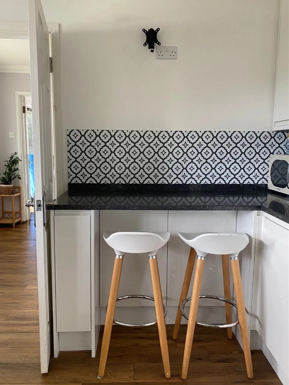 white gloss kitchen with karndean flooring and a granite worktop. There is a peel and stick tile backsplash above a breakfast bar and two bar stools