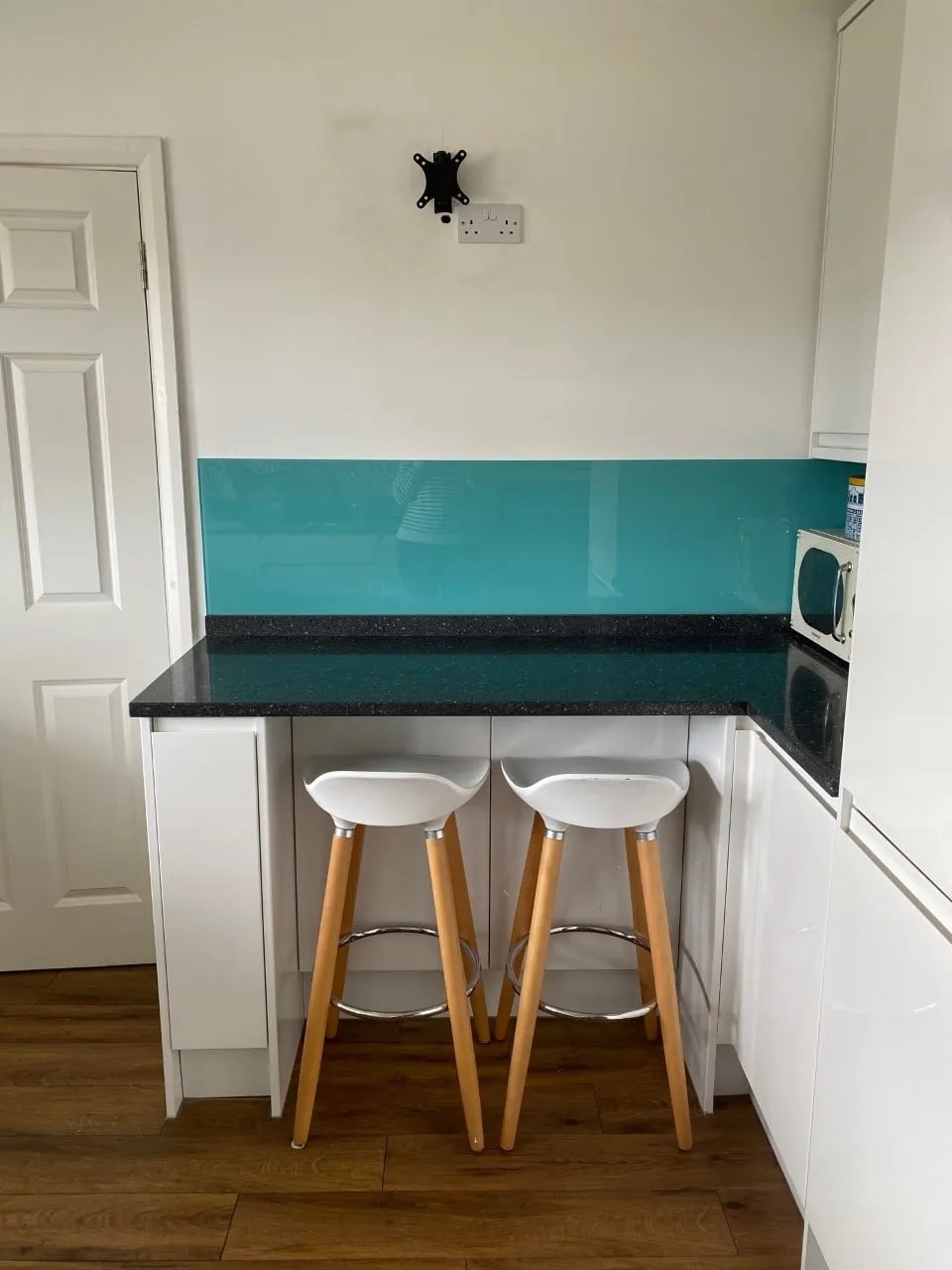 white gloss kitchen with karndean flooring and a granite worktop. There is a blue glass tile backsplash above a breakfast bar with bar stools