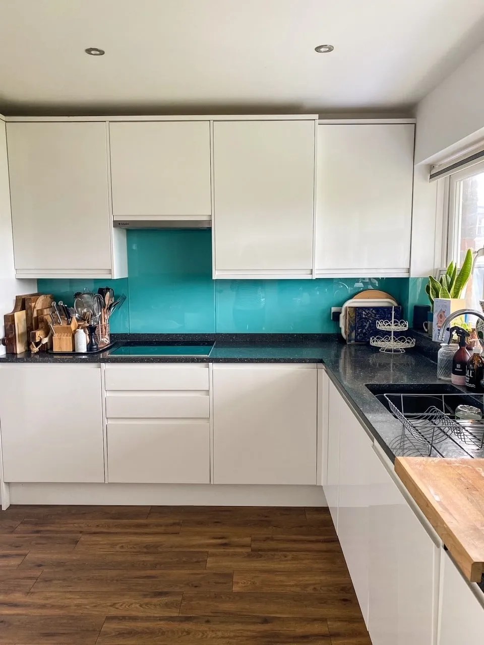 white gloss kitchen with karndean flooring and a granite worktop. There is a blue glass tile backsplash and a hob