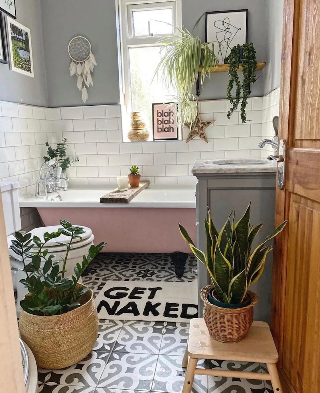 plants in a bathroom with patterned monochrome tiles, grey walls, metro tiles and a pink bath