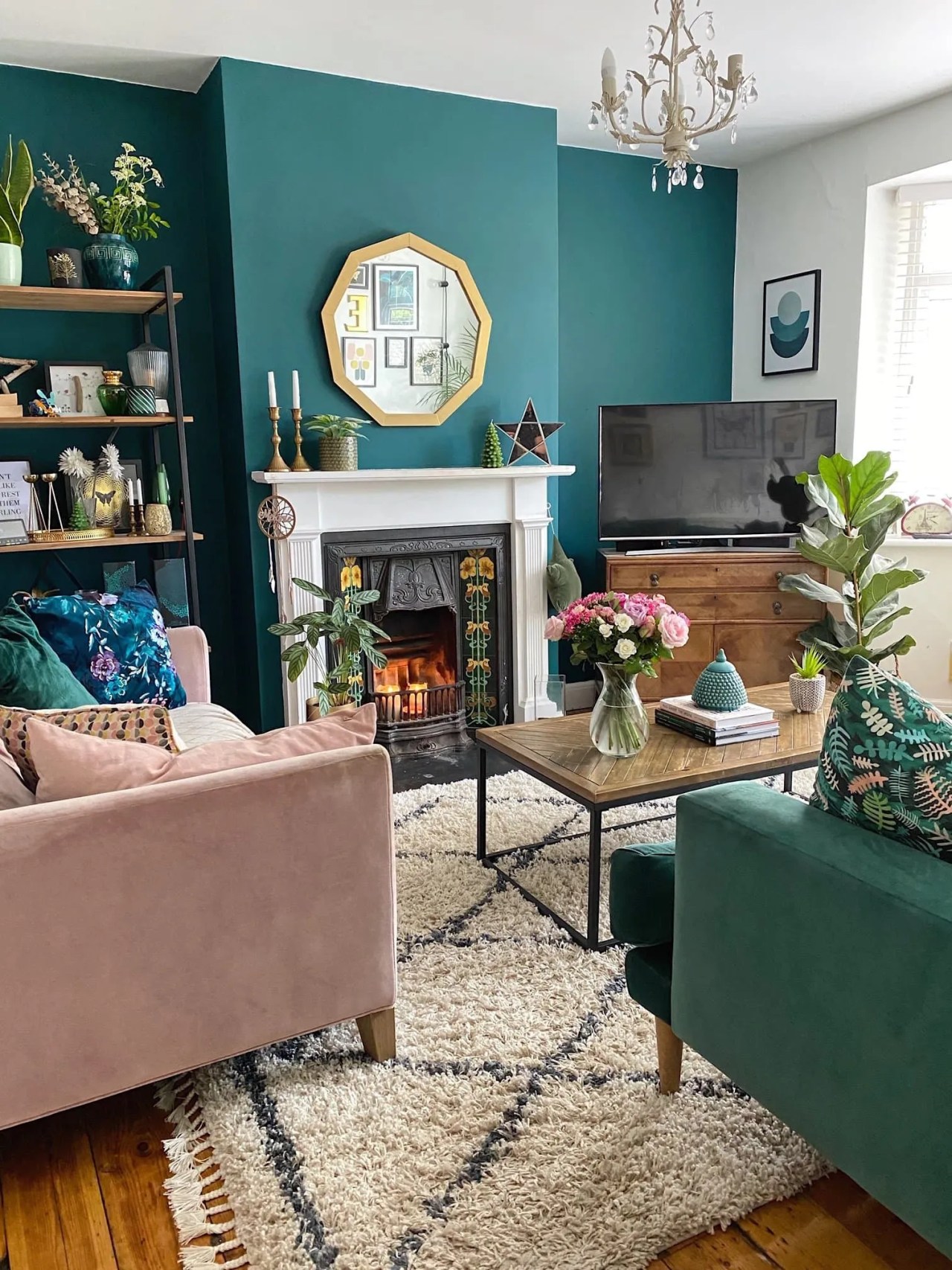 dark green walls in the living room with a fireplace. There are pink and green velvet sofas sat around an industrial style coffee table. 