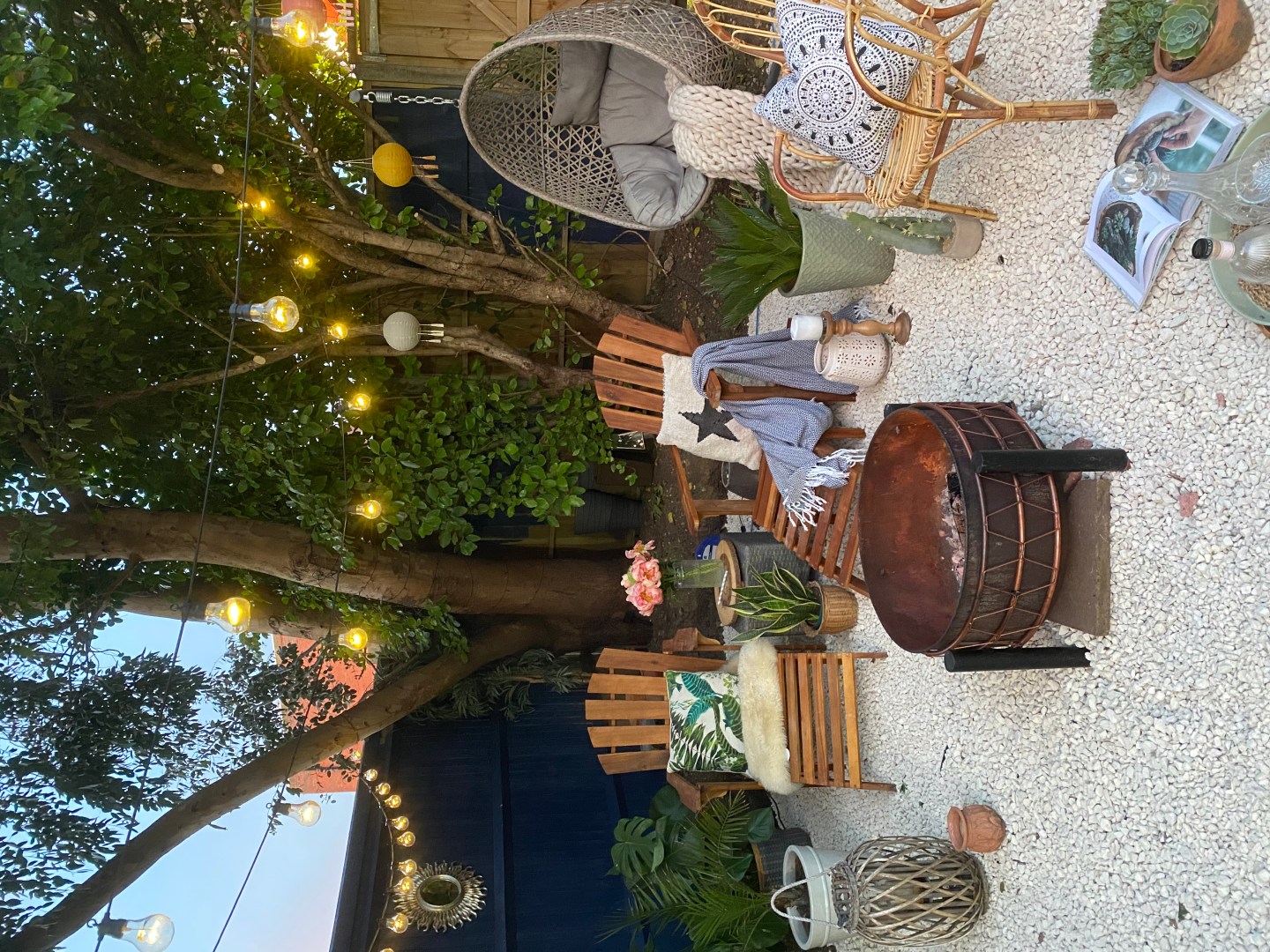 mediterranean garden with white gravel, blue fence, adirondack chairs and festoon lights