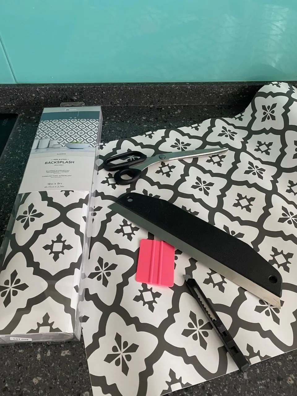 peel and stick tiles, scissors, wallpaper smoother and a knife laid out on a kitchen worktop