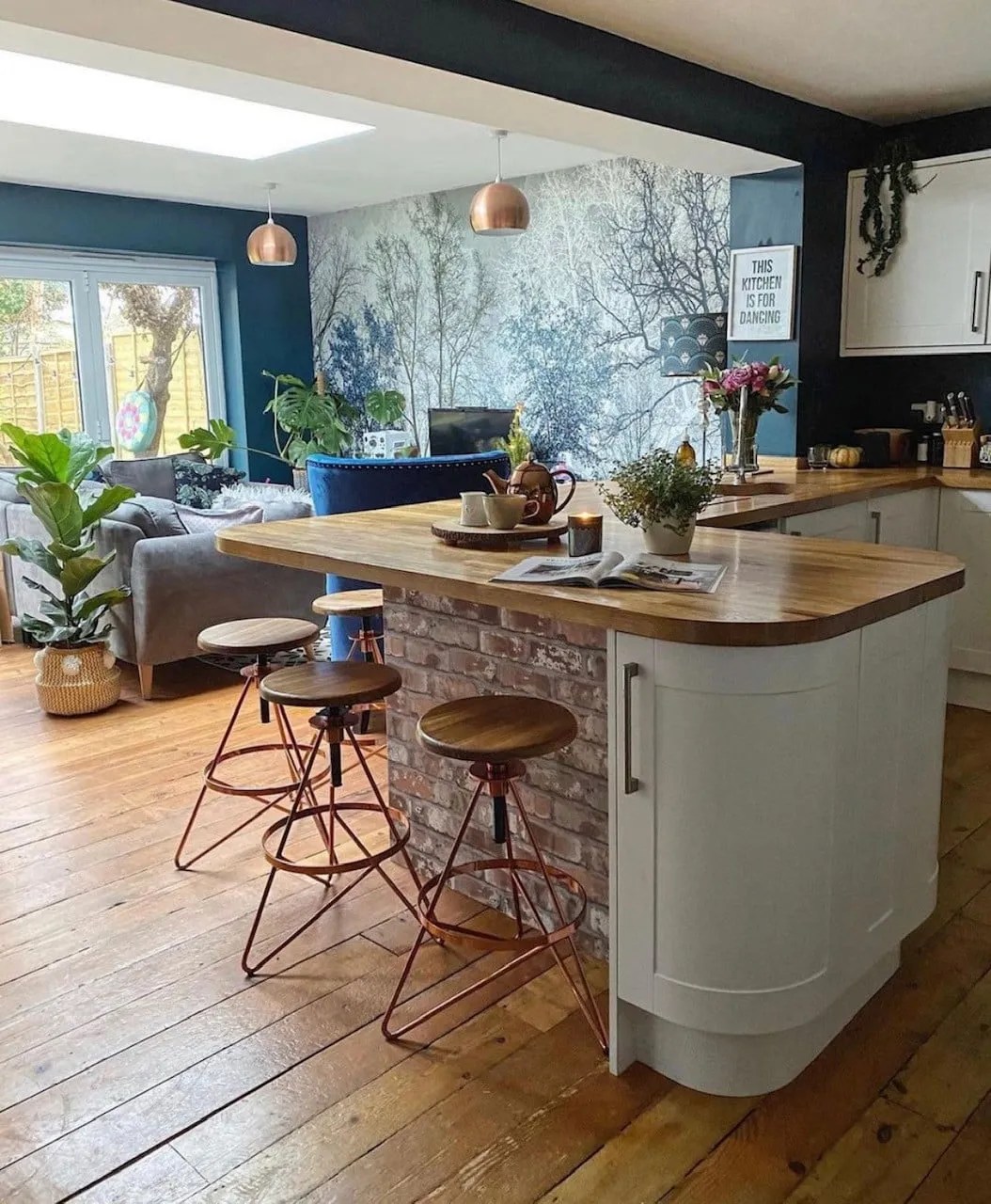 white shaker-style kitchen with a large woodland blue mural in the background. The walls are painted in Hague Blue and there are exposed pine flooring 