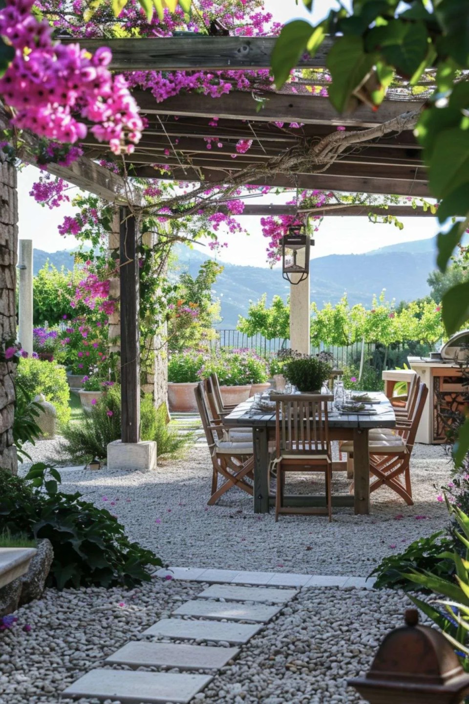 a garden dining table and chair set under a pergola in a mediterranean garden. There is bougainvillea growing up the pergola with olive trees in the background