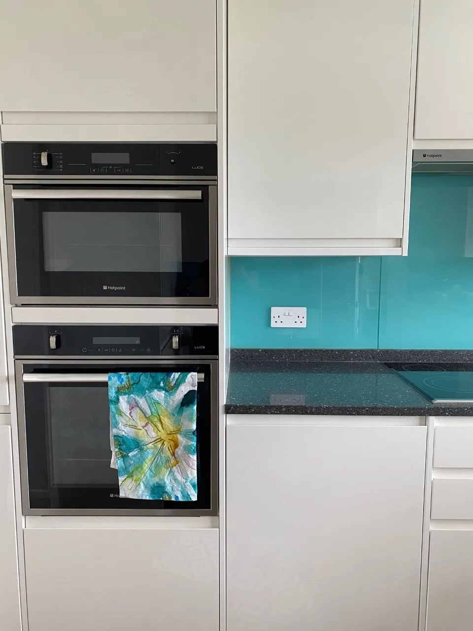 white gloss kitchen with a granite worktop. There is a blue glass tile backsplash and a hob and a double oven