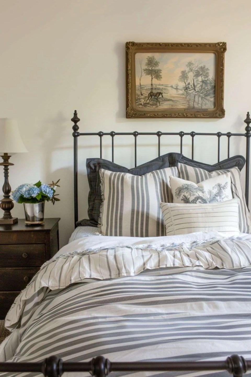 a wrought iron bed with striped bedding and vintage bedside table 